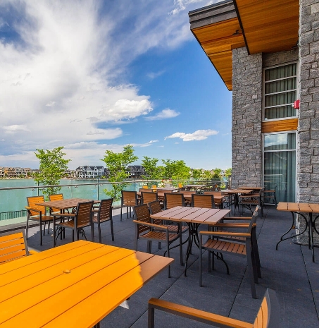 Outdoor seating area overlooking a serene lake, with homes in the distance, at Westman Village