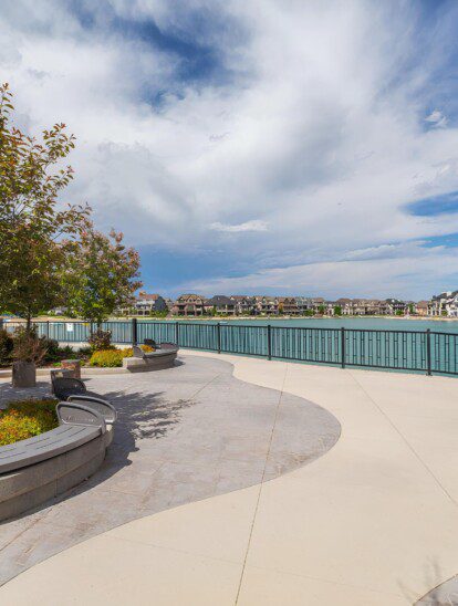 Scenic waterfront view of a senior independent living community in Calgary, with a paved walkway and seating areas
