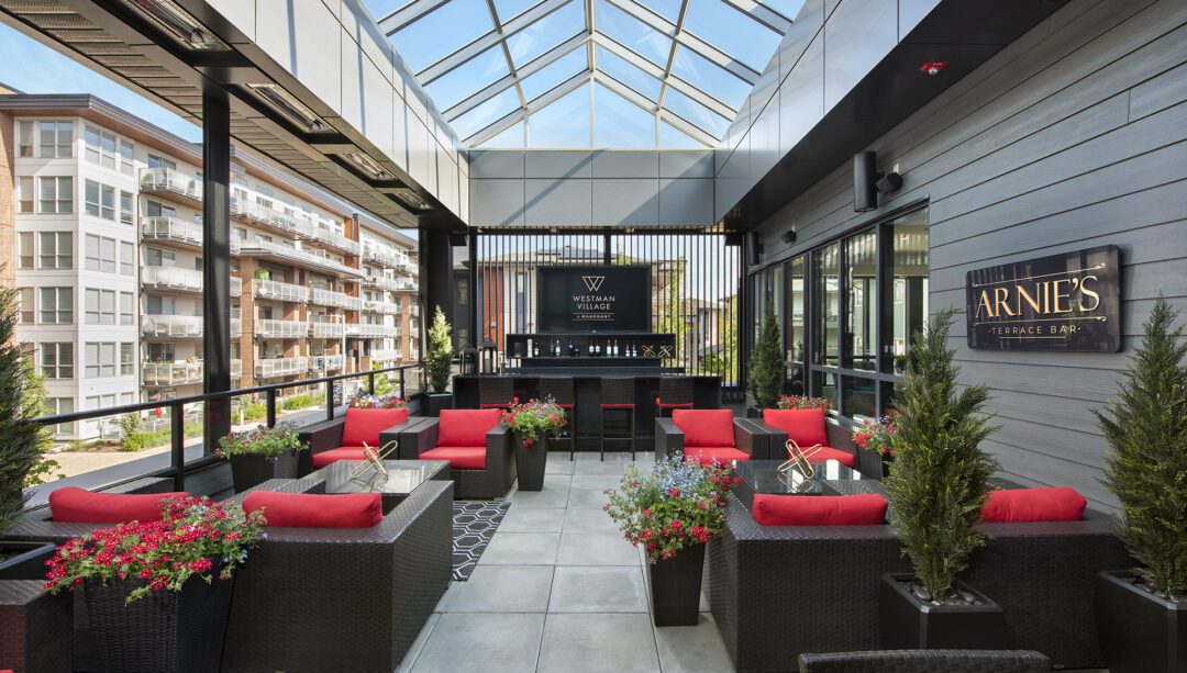 A rooftop patio with red accent seating, green plants, and a glass roof.