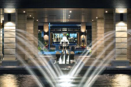 A lit courtyard with cascading fountains leading to the illuminated entrance of the Journey Club.