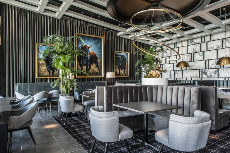 Chic restaurant interior with grey velvet seating, large bull artwork, and trendy lighting.