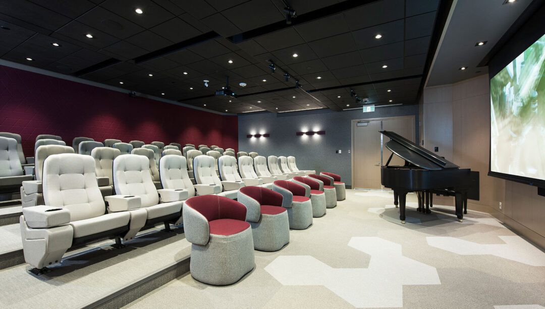A modern theater room with plush, white leather reclining seats and several round, red-and-gray ottomans. The atmosphere is upscale and cozy.