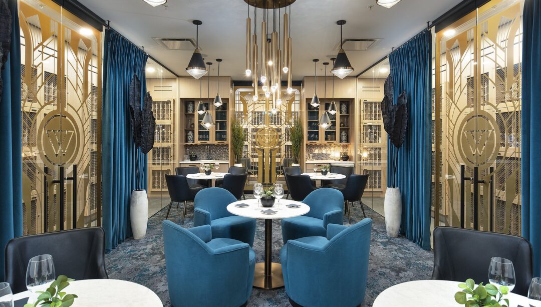 Elegant wine vault with plush blue chairs, golden shelves, and striking central chandelier.