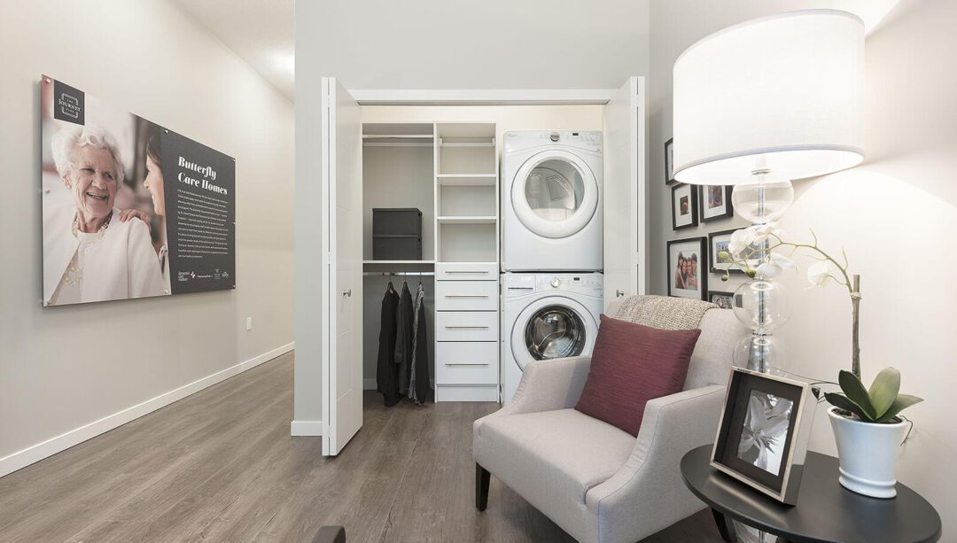 A memory care suite with a cozy chair, washer-dryer, and personal touches on the wall.
