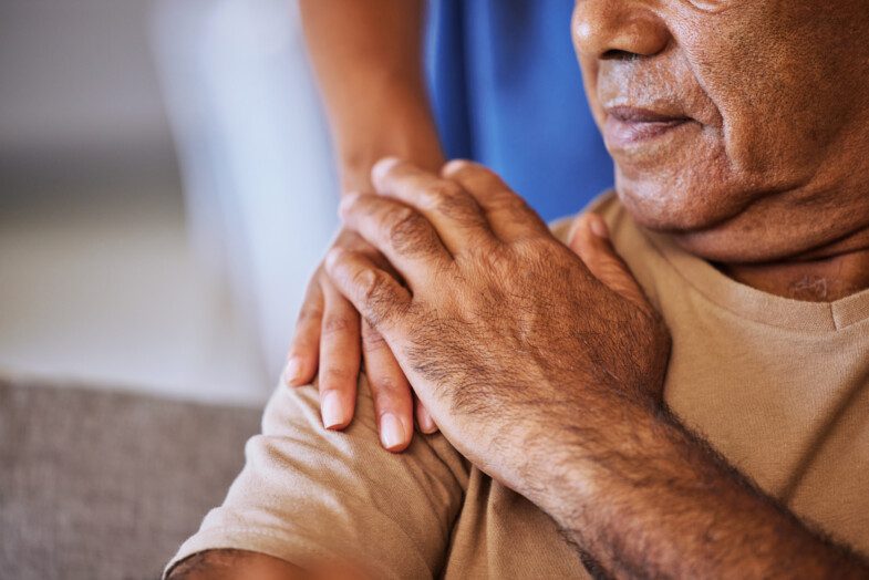 Close-up of a compassionate hand resting on the shoulder of an elderly person, offering support.