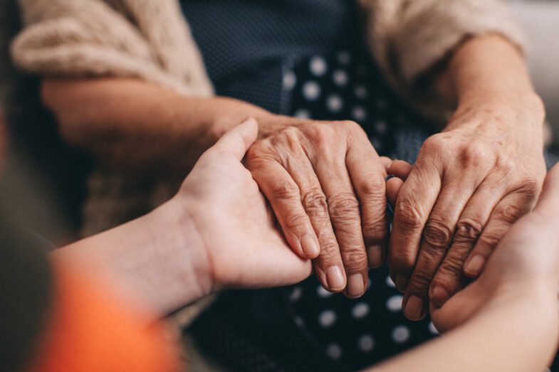 Close-up of a younger person's hands gently holding the aged hands of an elderly person.